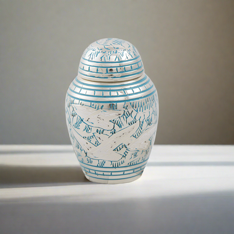 Small keepsake urn for ashes with intricate etched pattern of doves in flight with blue paint fill.