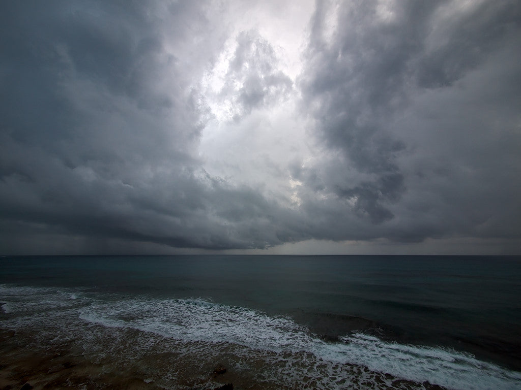 Dark clouds over the ocean with a foamy surf.