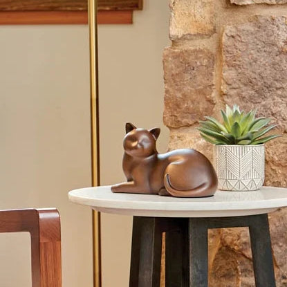 A brown figurine of a sleeping cat urn sits on a small round white side table in a transitional styled home.