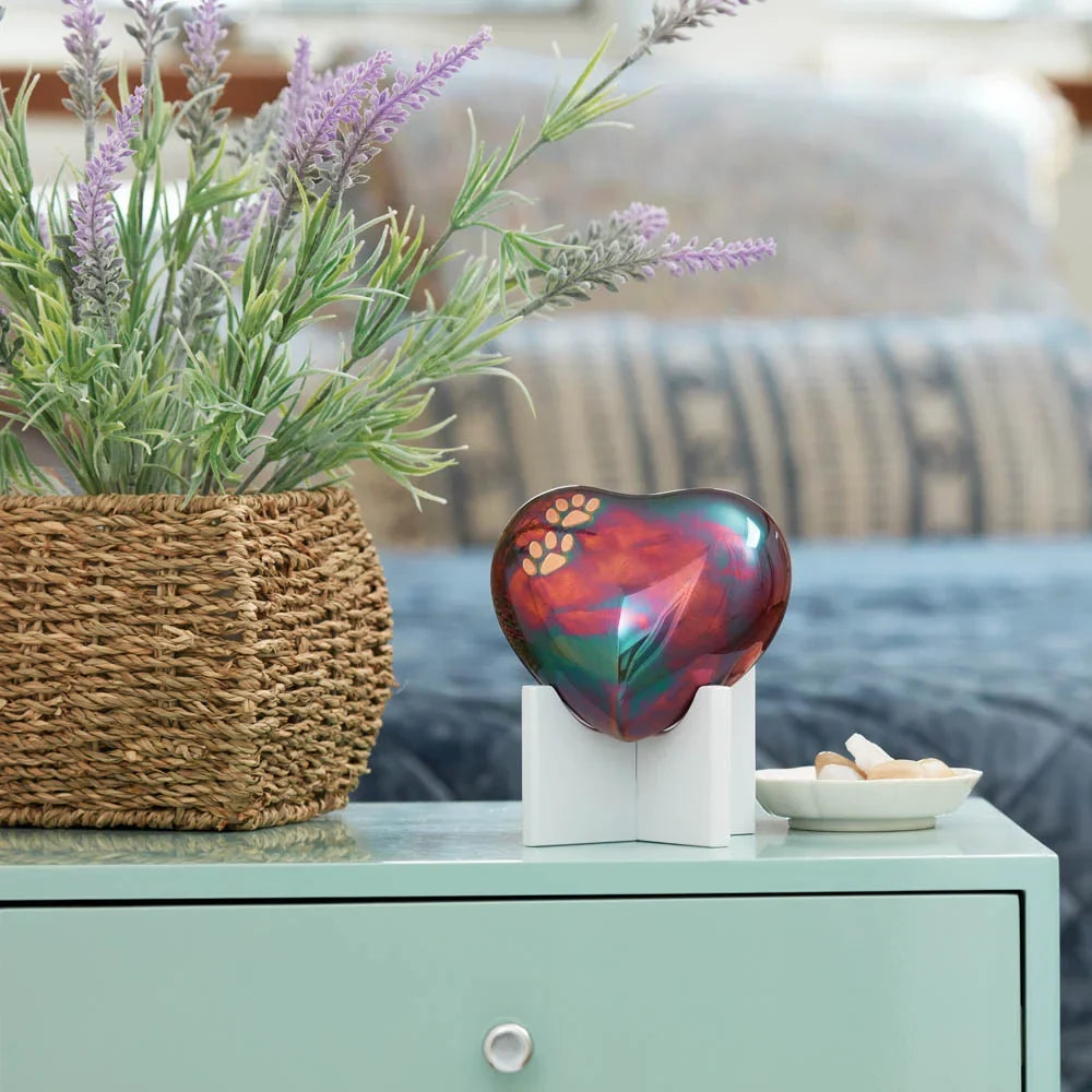 Decorative raku heart-shaped small pet keepsake urn on display in a home on a table with a plant and bowl in the background