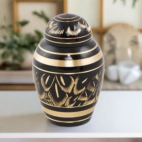 Beautiful black and gold keepsake urn for ashes with radiant etchings revealing an intricate pattern that resembles feathers.