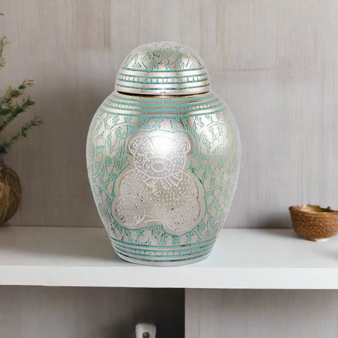 Urn for infants with intricately etched teddy bear and decorative pattern filled with light blue and white paint.