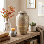 Traditional brass cremation urn in silver with hand etched gold floral motif in a home decor setting.
