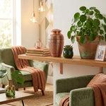 Classic brass urn with a polished copper finish featuring an elegant etched leaf design on a shelf. 