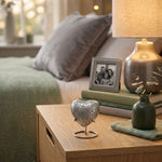 Metal heart-shaped memorial keepsake in a high gloss pewter finish featuring etched leaves in a heart stand in a home decor setting.