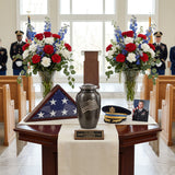 Metal cremation urn in a slate grey finish featuring a pewter American waving flag in a funeral service setting.