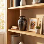 Slate grey pet urn with etched pewter paw prints wrapping around the urn in a home decor setting on a bookshelf.
