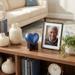 Metal heart cremation urn with a shimmery sky blue finish displayed with stand in a home decor setting.