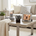 Brass heart  shaped dog cremation urn keepsake in a grey finish with silver paw prints displayed on a heart stand in a home decor setting.