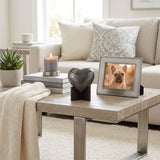 Brass heart  shaped dog cremation urn keepsake in a grey finish with silver paw prints displayed on a heart stand in a home decor setting.