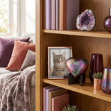 Raku heart for cremation ashes with beautiful green, pink, and purple shimmering finish with copper paw prints on a heart stand in a home decor setting.