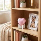 Pink heart dog urn with two silver paw prints in a home decor setting.
