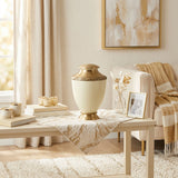Metal cremation urn featuring a shimmery pearl white finish, gold accents, and a floral band in a home decor setting.