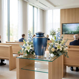 Modern metal urn in a dark blue, shimmery finish with pewter accents in a funeral service setting.