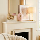 Metal cremation urn featuring a shimmering, soft pink finish, bronze accents, and a golden rose in a home decor setting.