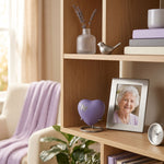 Metal heart-shaped cremation keepsake in a lavender finish featuring a silver butterfly silhouette, displayed in pewter heart standi in a home decor setting.
