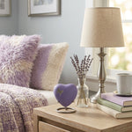 Metal heart cremation memorial urn in a lilac finish featuring a pewter butterfly silhouette, displayed in pewter heart standi in a home decor setting.