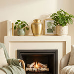Bronze memorial urn with bands showcasing delicate leaf patterns on a mantle above a fireplace.