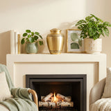 Bronze memorial urn with bands showcasing delicate leaf patterns on a mantle above a fireplace.