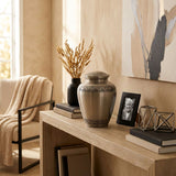 Traditional metal cremation urn featuring two etched leaf bands in a home decor setting.