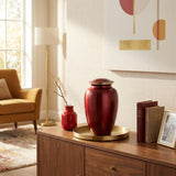 Red metal cremation urn in a traditional shape with gold accent in a home decor setting on a cabinet.