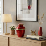 Red urn with metallic finish featuring a gold band in a home decor setting on a dresser.