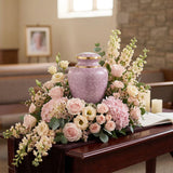Pink cloisonne cremation urn featuring a floral motif with gold accents in a funeral service setting.
