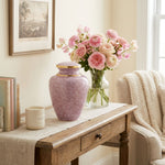 Pink cloisonne cremation urn featuring a floral motif with gold accents in a cozy home decor setting.
