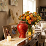 Metal cloisonne urn featuring red and orange leaves and flowers with gold accents in a home decor setting with photos.