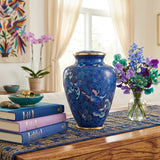 Blue cloisonne cremation urn with a butterfly pattern and floral design, sitting on a welcoming table styled with books and flowers.