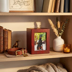 Wood photo urn with cherry veneer finish for pet on a bookshelf.