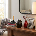 Small size black urn for ashes with pewter trim around the lid and three pewter bands around the body of the urn in a home decor setting.