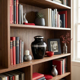 Small size black urn for ashes with pewter trim around the lid and three pewter bands around the body of the urn on a bookshelf.
