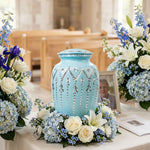 Light blue metal urn with hand etching in an intricate design in a funeral service setting.