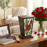 Red rose stained glass urn for cremation ashes with intricately cut glass pieces and a deep brown resin body in a home decor setting.