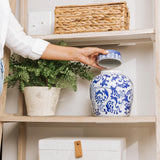 Hand holding blue and white ceramic cremation urn with ornate swirl pattern