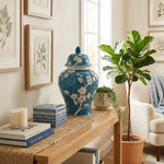 A blue ceramic urn in a ginger jar shape featuring a delicate plum blossom design in a home decor setting on a table.