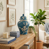 A blue ceramic urn in a ginger jar shape featuring a delicate plum blossom design in a home decor setting on a table.