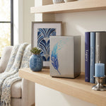 A metal cremation urn featuring a blue feather design that transcends into birds taking flight in a home decor setting.