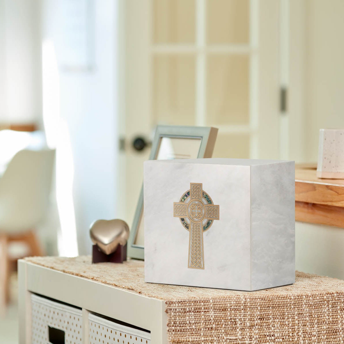 White natural marble urn with gold celtic cross and blue shell inlay on a table.