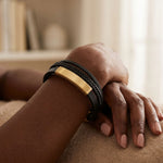 Feminine black braided leather bracelet with gold accents on a wrist.