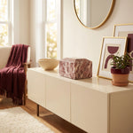 Pink, burgundy, and white natural marble box cremation urn in a home decor setting on a cabinet.