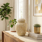 Beige natural marble urn with unique brown, white, and tan veining in a home decor setting on a table.