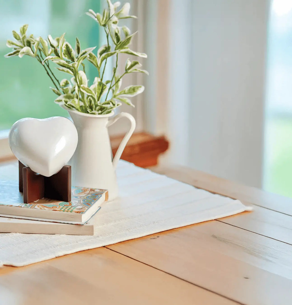 A white heart-shaped urn on a wooden stand, displayed on a light wood table.