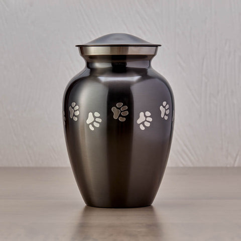 Slate grey pet urn with etched pewter paw prints walking around the urn and a sample of engraving on the front.